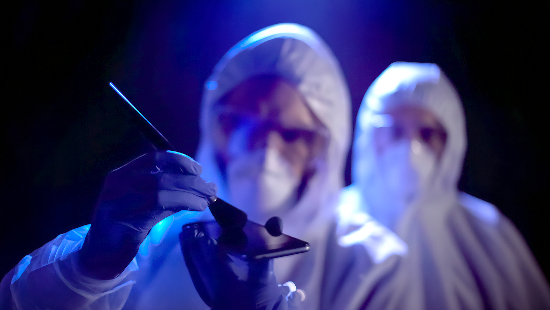 Two people in hazmat suits collecting fingerprints from cellphone.