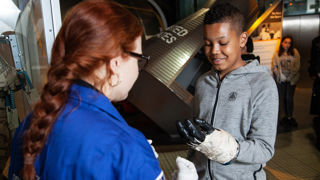 Education facilitator and teen in Into Space with an spacesuit glove science busk