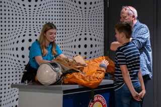 Science busk with a spacesuit is enjoyed by a young boy and Father