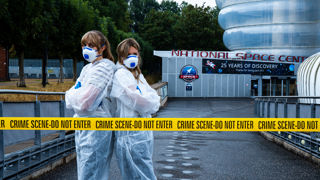 Laura and Sarah standing back-to-back behind a crime scene-do not enter sign